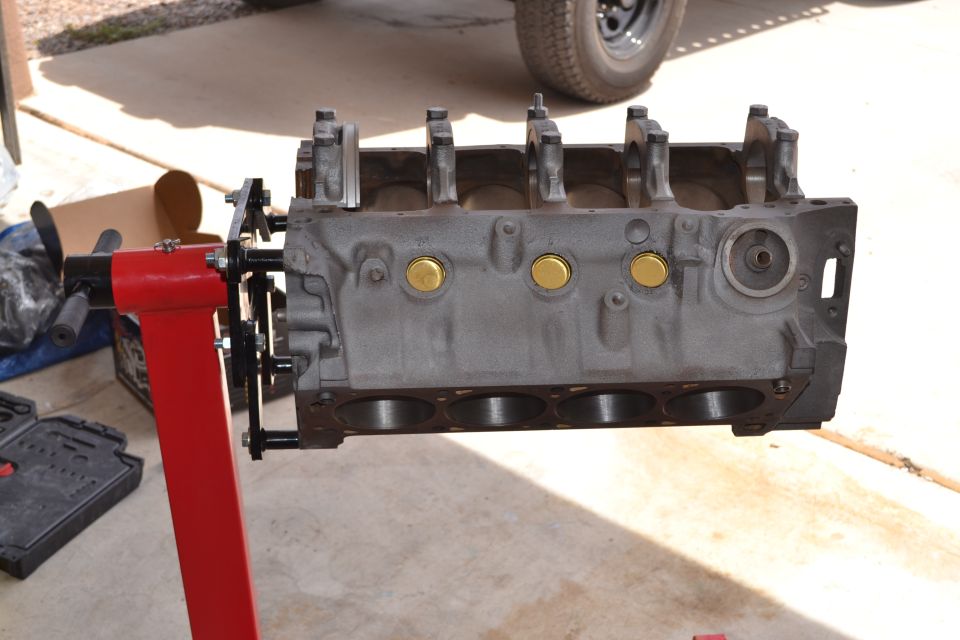 Engine block on a red engine stand, with a tire and part of a vehicle in the background