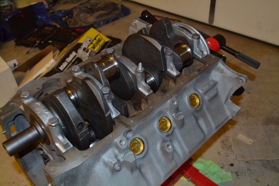 Engine block with crankshaft installed, showing bearing caps and gold-colored plugs