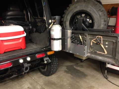 1987 Suzuki Samurai - The rear of an off-road vehicle is shown with a cooler, a propane tank, and a spare tire mounted externally.