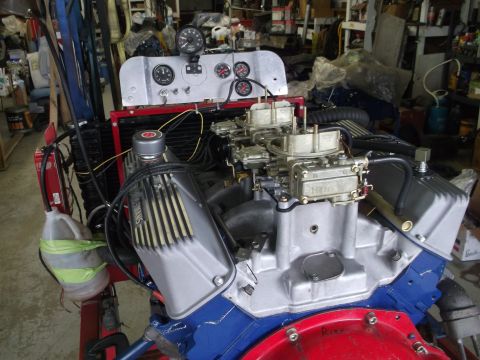 1967 Ford Mustang - Engine assembly with gauges and dual carburetors is displayed in a workshop setting.