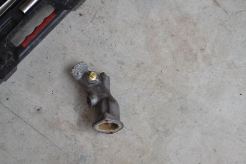 1981 Ford F-250 - A metal thermostat housing is shown on a concrete surface next to a tool case.