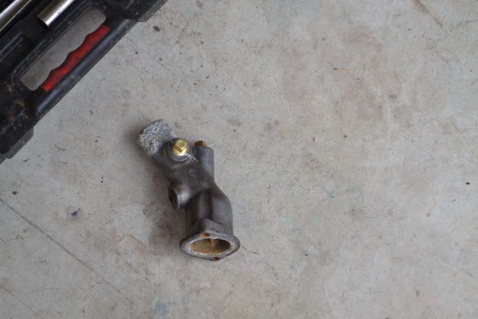 Thermostat housing with a brass bolt and a tool case in the background