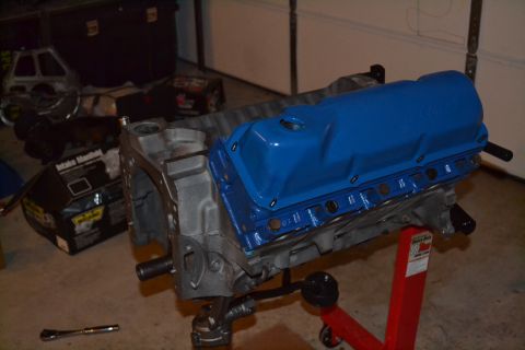 1981 Ford F-250 - Engine block and blue valve cover on an engine stand, with a box of intake manifold parts nearby.