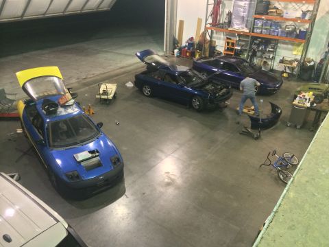 1995 Ford Probe - Multiple vehicles are in a garage, with one sports car undergoing work and another with its hood and hatch open.