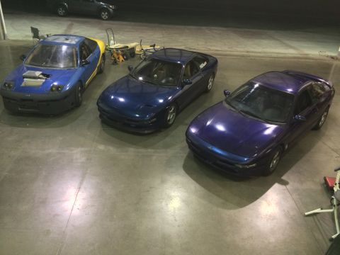 1995 Ford Probe - Three Ford Probe cars are parked in a garage, with one modified with a hood scoop and yellow rear.