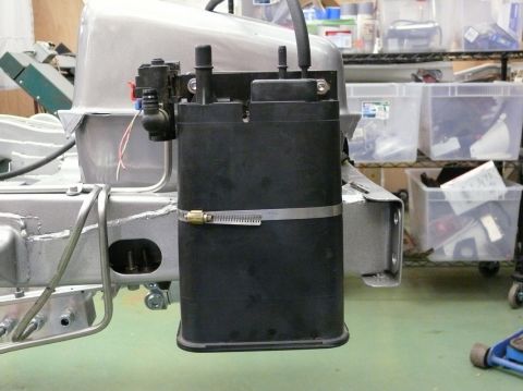 Black plastic fuel canister with metal hose clamp attached to vehicle frame