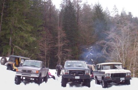 1982 Ford Bronco - A group of off-road vehicles are gathered in a snowy, wooded area.