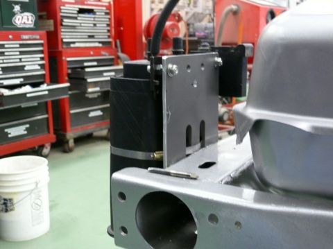 Close-up of a black cylindrical part mounted to a metal bracket, with a silver fuel tank visible on the right.
