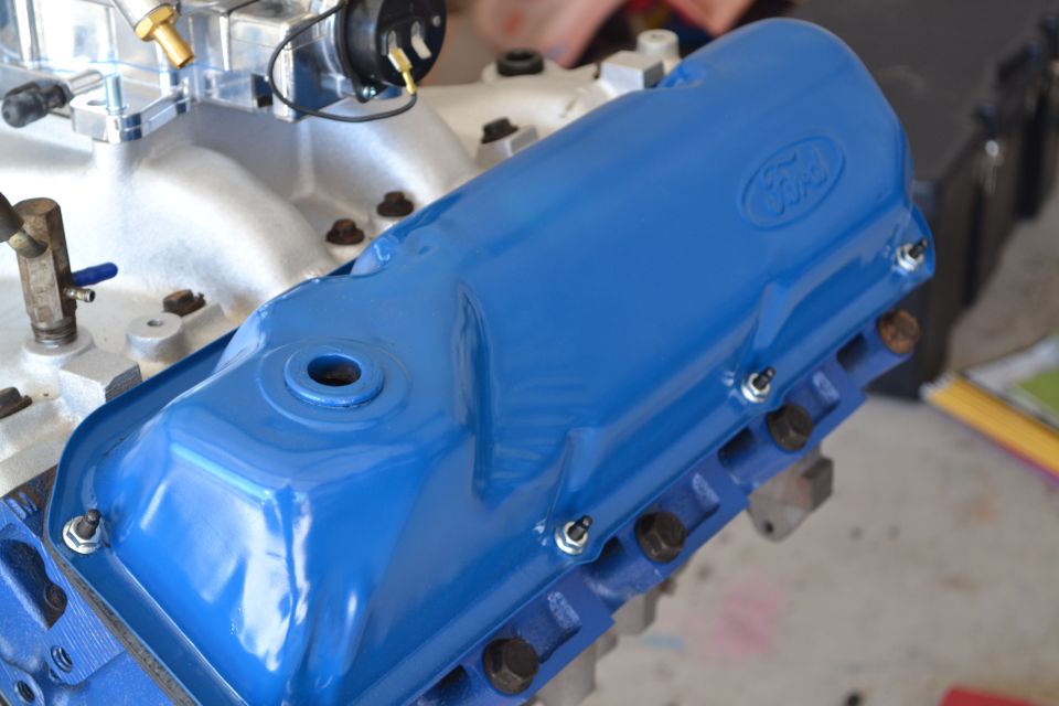 Blue Ford valve cover on an engine block, showing bolts and part of the intake manifold