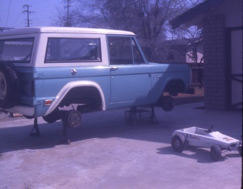 1996 Ford Bronco - A classic Ford Bronco is elevated on jack stands in a driveway, undergoing maintenance.