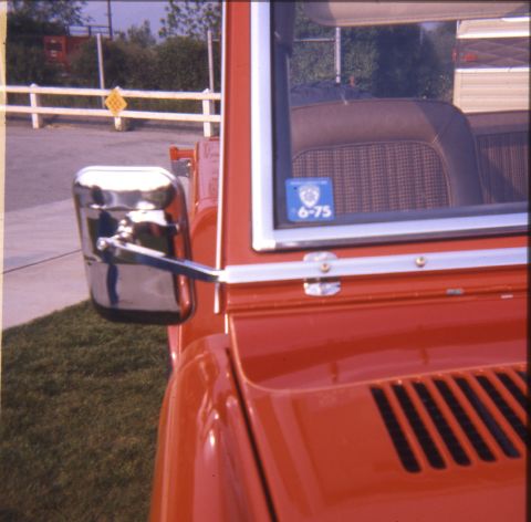 1996 Ford Bronco - A red Ford Bronco is seen from the front three-quarter angle, with a visible side mirror and a sticker on the window.