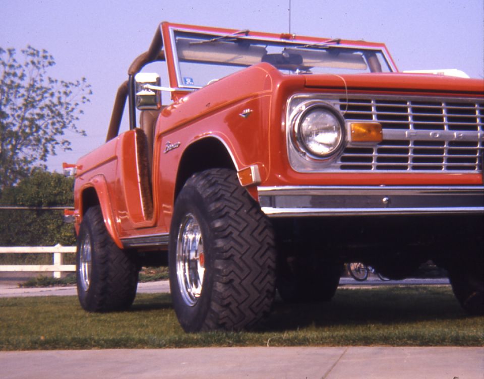 Red Ford Bronco with chrome wheels and large tires, viewed from a low angle