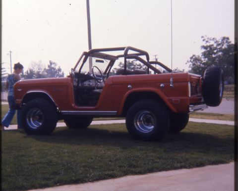 1996 Ford Bronco - This red convertible SUV is seen from the side, a roll cage and a spare tire mounted on the rear.