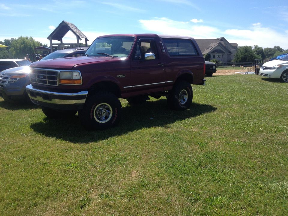 Maroon 1996 Ford Bronco with chrome trim and aftermarket wheels parked on grass