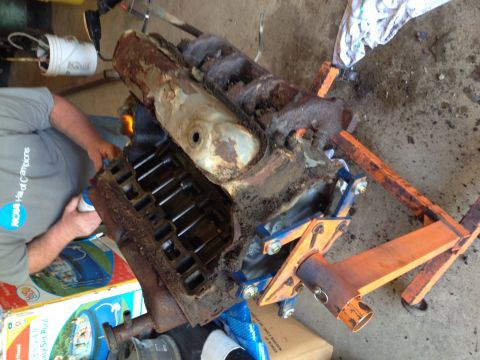 1996 Ford Bronco - A heavily rusted engine block is mounted on an engine stand, with a person working on it in the background.