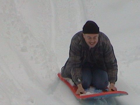 1982 Ford Bronco - A man wearing a plaid shirt and beanie enjoys a ride down a snow-covered slope on a sled.
