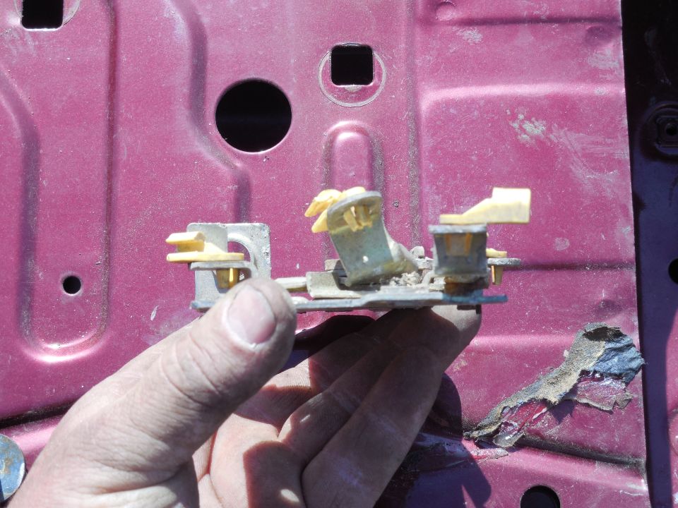 Hand holding metal bracket with yellow clips against maroon panel