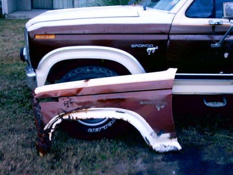 1980 Ford Bronco - A detached, heavily damaged fender lies in front of a brown and white 1980 Ford Bronco.