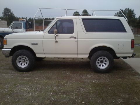 1990 Ford Bronco - Side profile of a white 1990 Ford Bronco parked outdoors with another truck in the background.