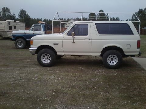 1990 Ford Bronco - Side view of a white 1990 Ford Bronco and a blue Ford pickup truck parked outdoors.