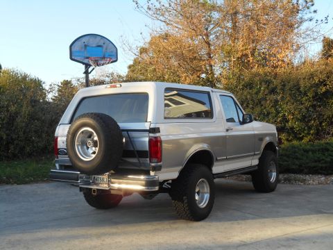 1994 Ford Bronco - The rear of a two-tone Ford Bronco is parked outside with a basketball hoop in the background.