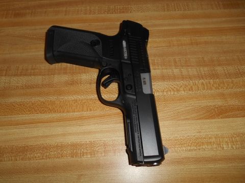 1994 Ford Bronco - Black semi-automatic pistol with textured grip and visible serial number on a wood-grain surface.