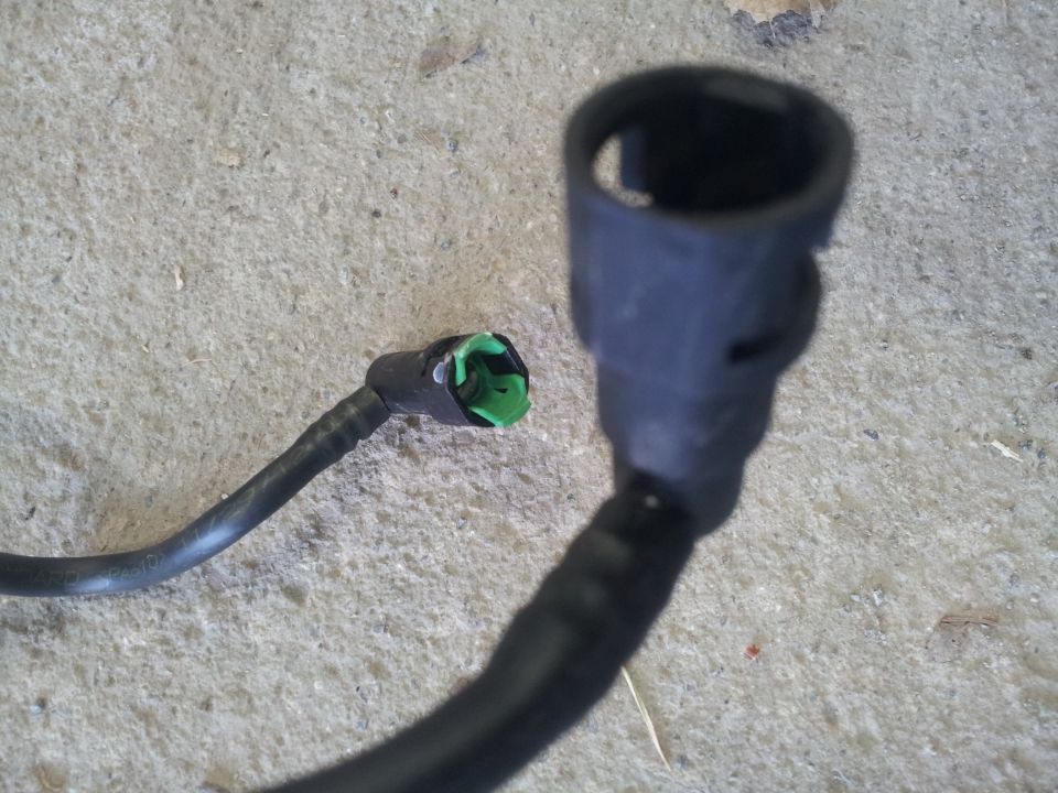 Two black fuel line connectors with green inserts on a concrete surface