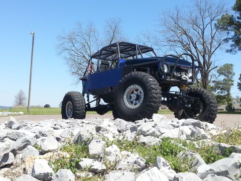 1967 Ford Mustang - Custom off-road buggy with a roll cage and oversized tires sits on a pile of rocks under a clear blue sky.