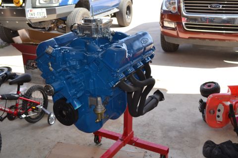 1981 Ford F-250 - A blue V8 engine is displayed on a red stand, with other vehicles partially visible in the background.