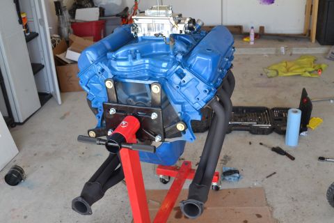 1981 Ford F-250 - A blue V8 engine is mounted on a red engine stand, with tools and supplies scattered around the garage floor.