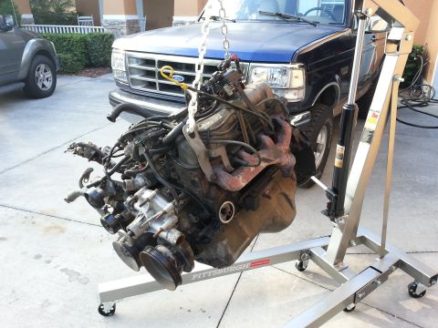 1994 Ford Bronco - Engine hoist lifting an engine in front of a blue Ford truck, likely from the early to mid-1990s.