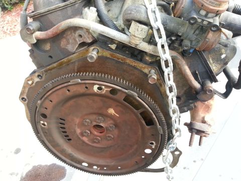 1994 Ford Bronco - Engine block and flywheel assembly with a metal chain attached.