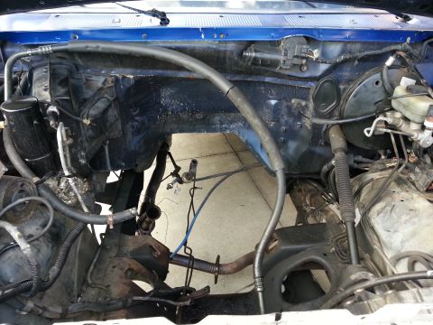 1994 Ford Bronco - The engine bay of a blue vehicle is shown with various components removed, revealing the internal structure.