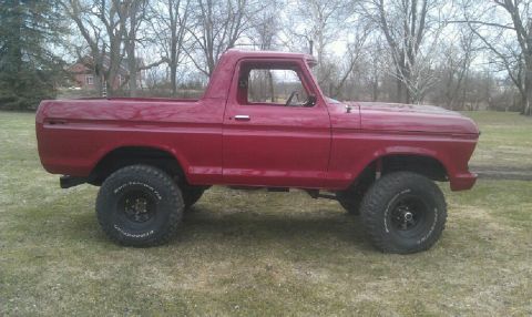 1978 Ford Bronco - A red pickup truck is parked on a grassy field with trees in the background.