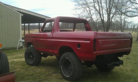1978 Ford Bronco - A red 1978 Ford Bronco sits in a grassy yard next to a building, its top removed and suspension lifted.