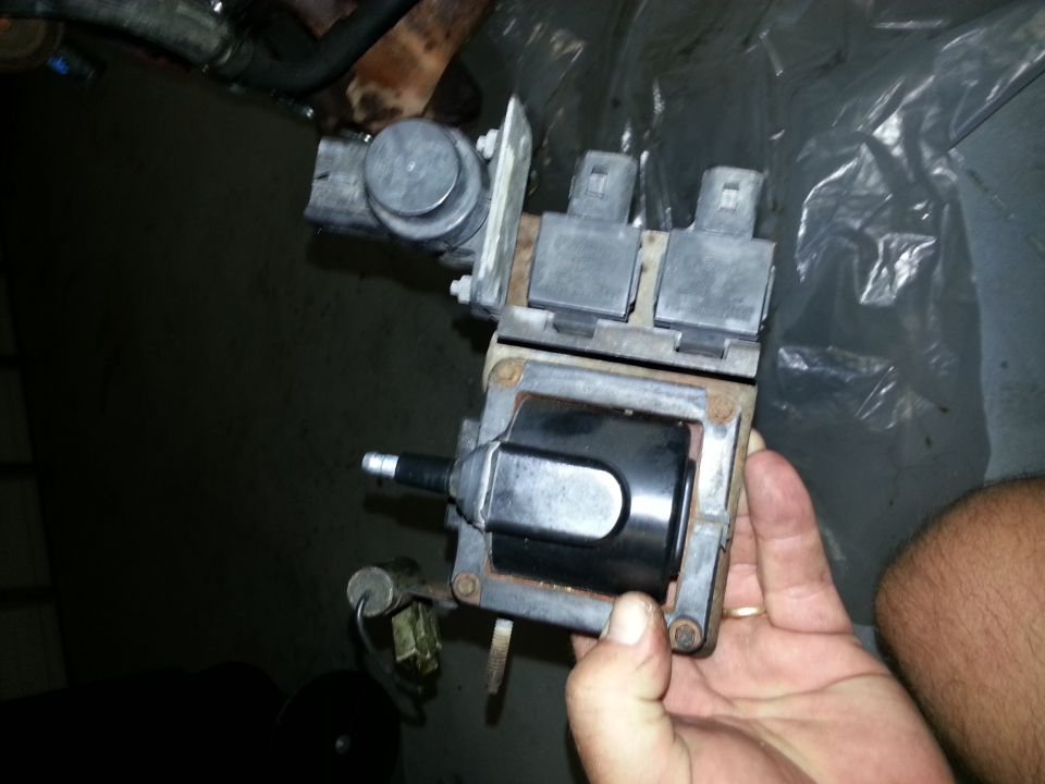 Hand holding a black ignition coil pack with electrical connectors