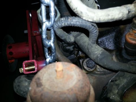 1994 Ford Bronco - Close-up of an engine component with a chain and red jack attached, suggesting mechanical work.
