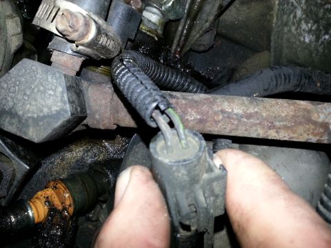 1994 Ford Bronco - Close-up view of engine components, showing a hand disconnecting a wiring harness from a fuel injector.