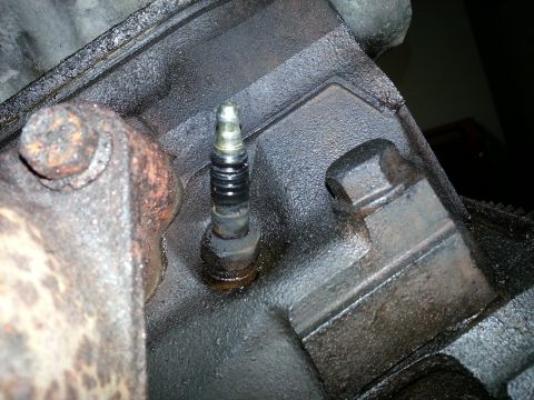 1994 Ford Bronco - A close-up of a spark plug installed in a heavily oiled engine block.