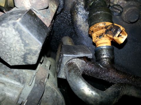 1994 Ford Bronco - Close-up view of a dirty engine fuel injector, showing grime and oil buildup on the component.