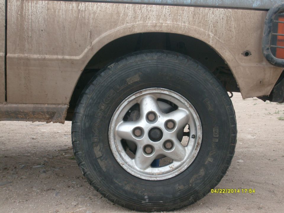 Close-up of a 1991 Land Rover Range Rover's front wheel and fender, covered in dirt