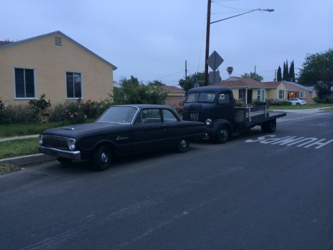 1968 Ford Mustang - A 1960 Ford Falcon sedan is parked on the street next to a flatbed truck.