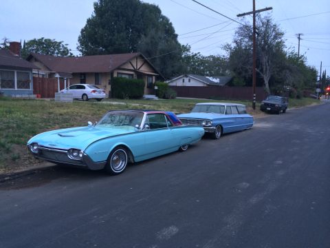 1968 Ford Mustang - A light blue 1965 Ford Thunderbird convertible is parked on the street next to a blue station wagon.