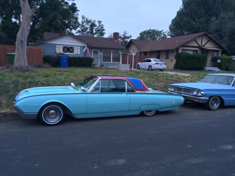 1968 Ford Mustang - A light blue 1960 Ford Thunderbird with a two-tone roof is parked on a street next to another classic car.