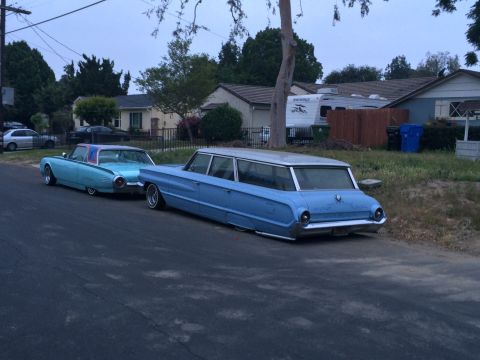 1968 Ford Mustang - Two vintage cars are parked on a residential street. The station wagon is a long, light blue vehicle.