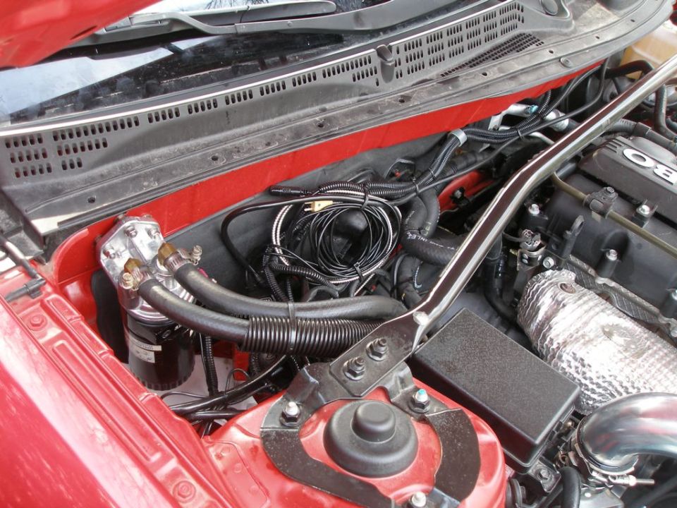 Red engine bay with oil cooler, wiring, and strut bar. Text reads 'SUPERMOTORS.NET'