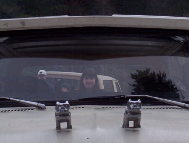 View through truck windshield of two chrome bulldog hood ornaments with a smiling woman inside
