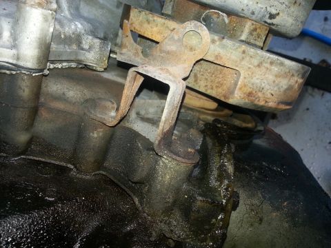1994 Ford Bronco - A rusty bracket is attached to a greasy transmission housing, suggesting an engine component needing attention.