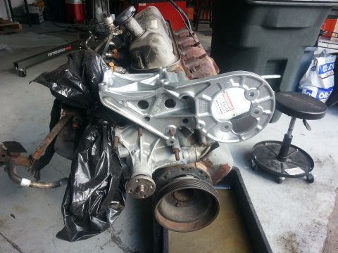 1994 Ford Bronco - Engine assembly with a silver bracket and black plastic covering, possibly for a Ford Bronco.