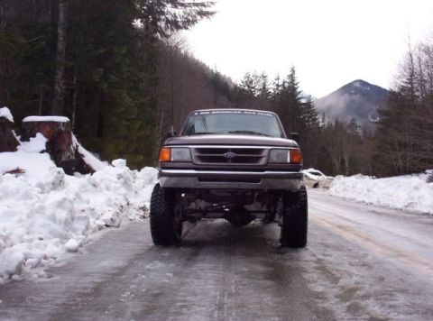 1982 Ford Bronco - A lifted brown Ford Ranger pickup truck is parked on a snowy and icy road with trees and a mountain in the background.